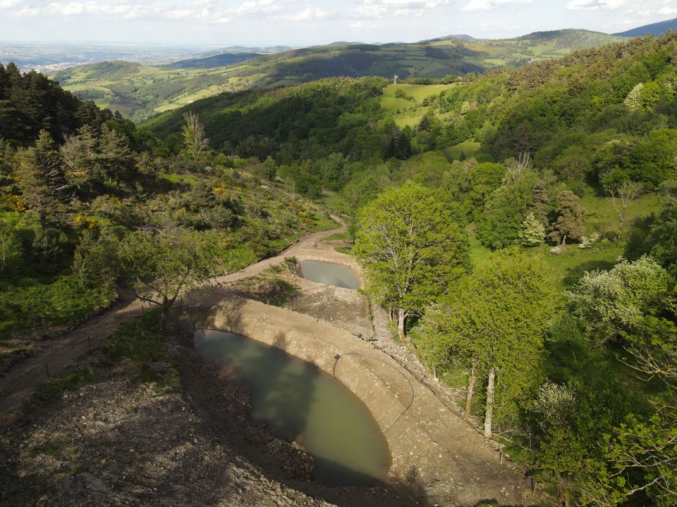 Deux retenues d'eau creusées à flanc de coteau, en contrebas d'un chemin de terre ; au-delà, les vallons boisés du massif et la plaine au loin.